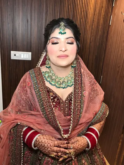 A beautiful bridal portrait. The bride is wearing a maroon velvet lehenga with a heavy green beaded kundan necklace.