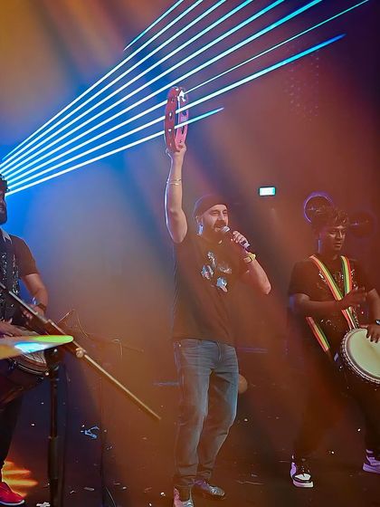 A duplicate of 114, holding up a tambourine while performing with live drummers.