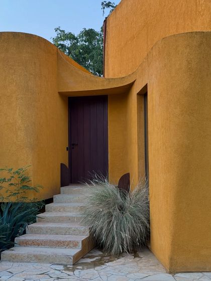 The entrance to one of our suites, where the heavy wooden door contrasts with the soft, textured walls and wild ornamental grass.