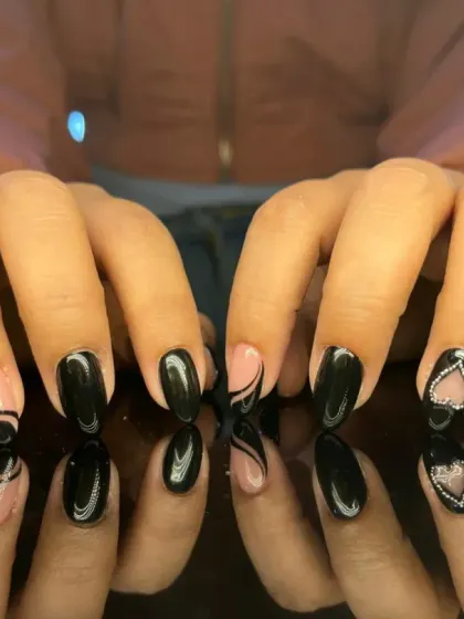 A sleek and sexy black manicure with negative space swirls and a sparkling rhinestone heart accent.