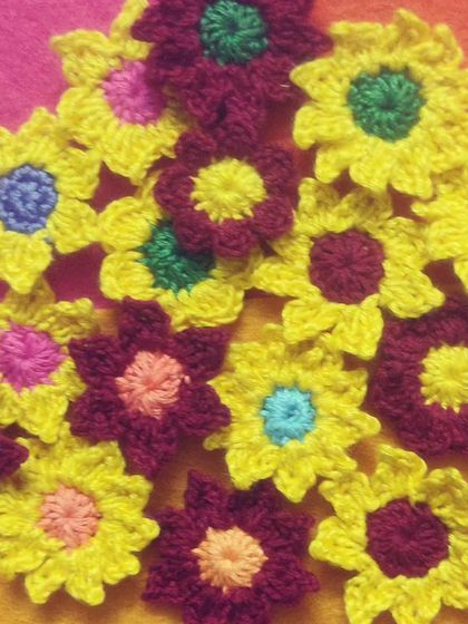 A pile of colorful crochet flower appliqués. These little blooms are perfect for embellishing bags, clothes, or any other craft project you can dream of.