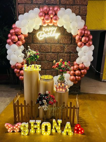 A beautiful ring backdrop with rose gold and white balloons, surrounded by floral arrangements and marquee letters for a personalized touch.
