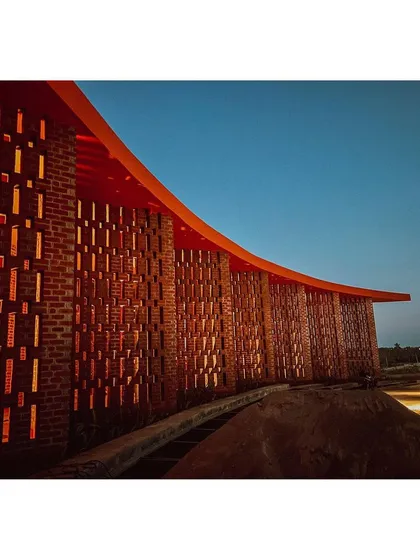 The brick jali wall glows at night, transforming the building into a lantern and a landmark for the community.