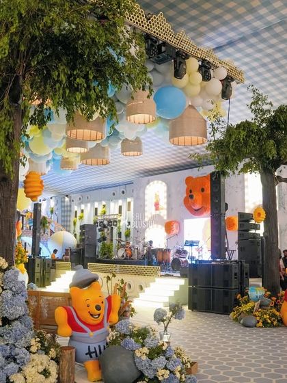 A wide view of the Hundred Acre Wood, brought to life for a first birthday. The space features large trees, a ceiling of balloons, and beloved characters like Winnie the Pooh.