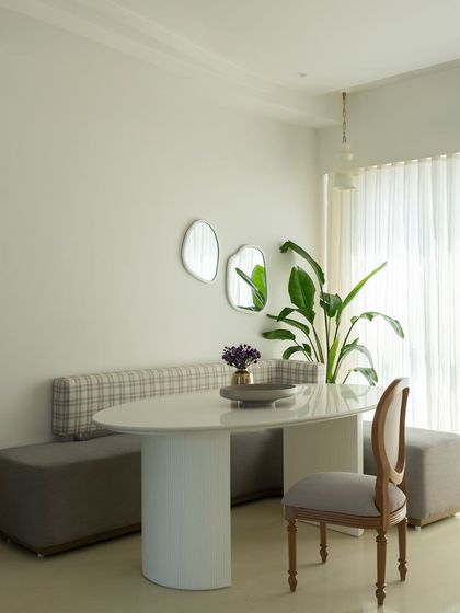 This minimalist dining nook is designed for quiet meals. A built-in bench with plaid upholstery is paired with a simple pedestal table and a classic wooden chair. The organic-shaped mirrors on the wall add a touch of artistry and reflect light.