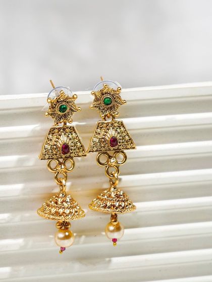 Traditional gold jhumka earrings shot in a bright, high-key style on a white textured background. This makes the product look fresh and modern.