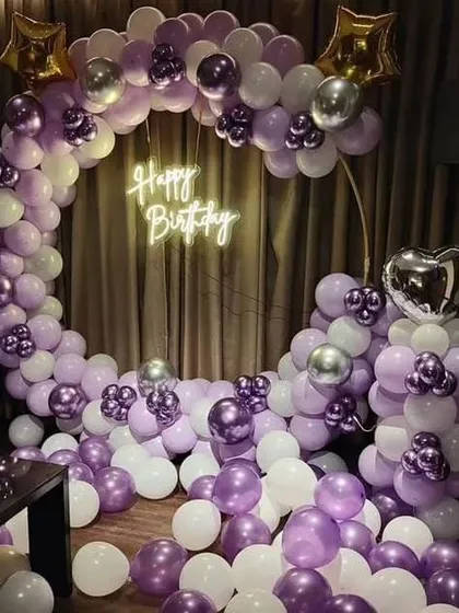 An elaborate ring decoration with purple, white, and silver chrome balloons. The floor is filled with balloons, creating an immersive and luxurious photo corner.
