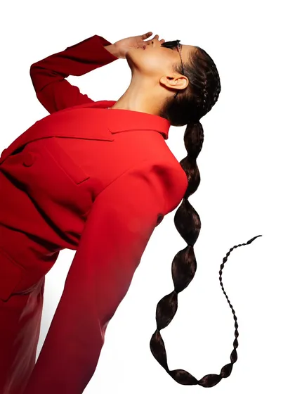 A high-fashion, graphic image for a power-suiting brand. The model's dramatic pose and the unique, bubble-ponytail hairstyle create a visually striking and memorable shot.