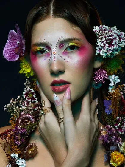 A highly creative look featuring colorful, artistic makeup and a headpiece made of various flowers. This is where makeup becomes wearable art.