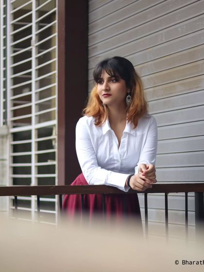 A thoughtful, looking-away pose on an urban balcony. The clean lines of the building create a minimalist backdrop.