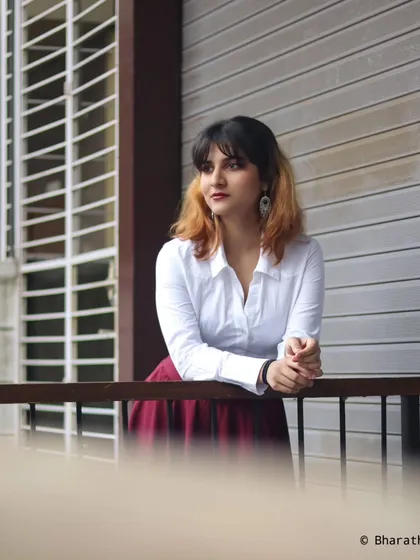 A pensive, looking-away shot of the model in the same outfit. The composition uses the balcony railings to frame the subject.