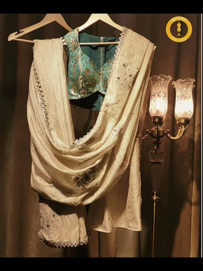A beautiful contrast of a teal embroidered blouse against a cream-colored saree. This flat lay highlights the artistry of the hand-tailored blouse.