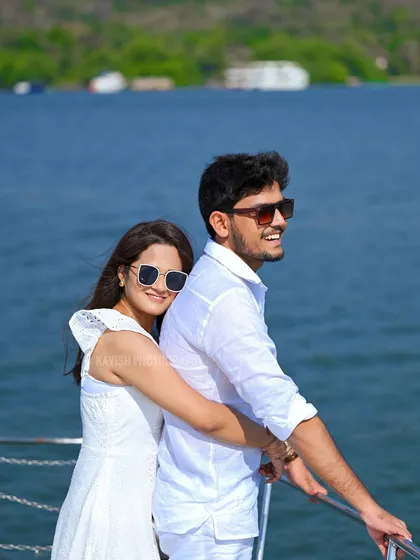 A stylish couple portrait on a boat, looking out over the water. Their coordinated white outfits and sunglasses give this pre-wedding shot a chic, modern feel.