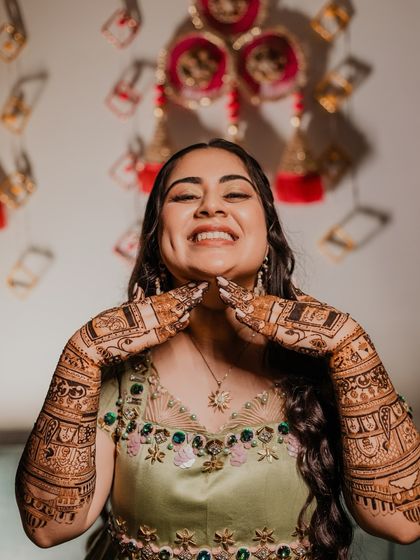 A joyful, candid shot of the bride showing off her henna-adorned hands with a big smile.