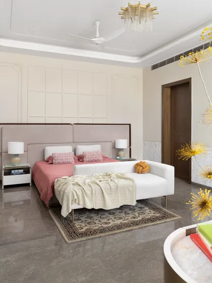A serene bedroom in the "Ideal Home" project, featuring a soft, neutral palette with pops of pink. The elegant wall paneling and contemporary chandelier add a touch of classic luxury.