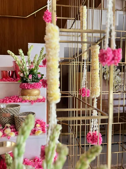 A view of the festive staircase decor through a modern golden railing. Hanging floral tassels of jasmine and pink carnations add a delicate touch to the grand floral arrangements on the steps.