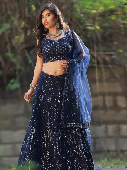 A full-length portrait of the 'Sapphire from Heeramandi' look. The deep blue of the lehenga is captured against a natural stone wall, showing how the outfit looks in an outdoor setting.