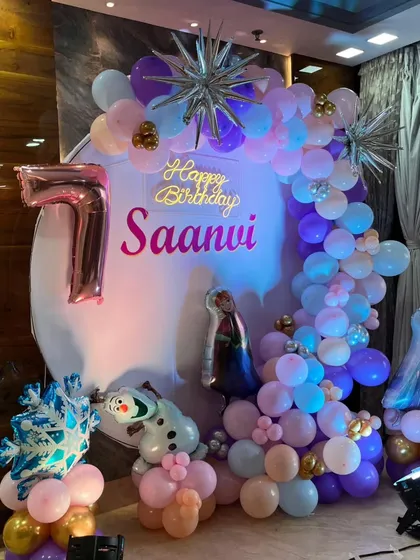A magical Frozen theme for a 7th birthday party. The decor includes a custom ring backdrop, character cutouts, and a large pink foil '7' balloon.
