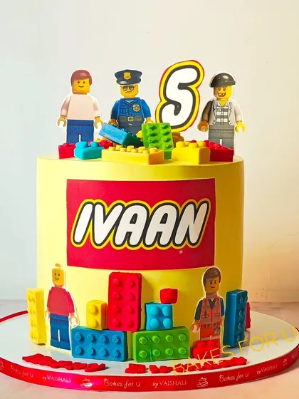 A vibrant Lego-themed cake with the birthday boy's name in the iconic Lego font. The cake is decorated with edible Lego figures and colorful chocolate blocks.
