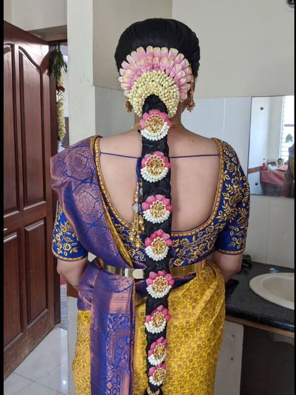 A vibrant bridal look with a traditional braid decorated with pink and white flowers and matching 'Jada Billa' ornaments.