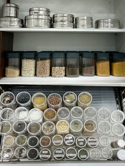 A top-down view of a perfectly organized spice drawer alongside a cabinet of decanted dals. This combination of storage solutions makes every part of the cooking process more efficient and enjoyable.