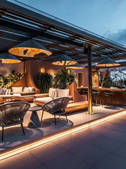 A wide evening shot capturing the full ambiance of the illuminated terrace. The lighting design accentuates the architectural forms and lush plantings, creating a dramatic and magical nighttime environment.