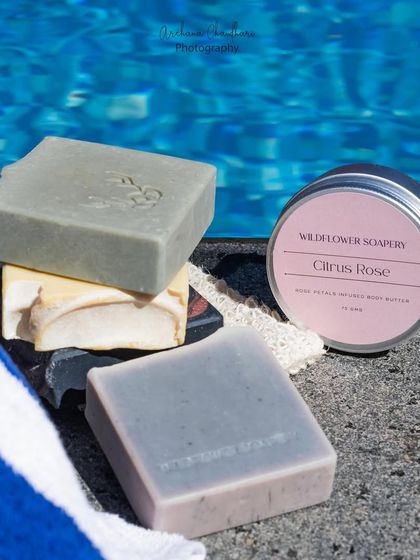 A close-up of a stack of colorful handmade soaps next to a tin of body butter. This composition is great for showing product variety in a single, cohesive image.