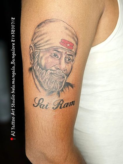 A realistic portrait tattoo of Sai Baba with "Sai Ram" scripted below, a popular piece for devotees.