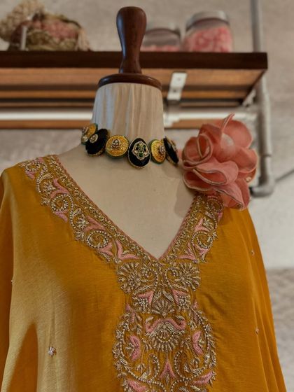 A close-up of a beautifully embroidered neckline on a yellow kaftan, paired with a unique, handcrafted choker.