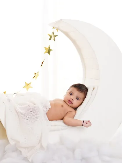 A peaceful baby lying on a moon prop under a soft blanket, with a string of golden stars overhead. A magical setup for a baby photoshoot.