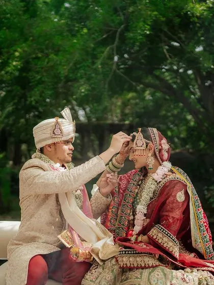 A sweet moment during the ceremony, with the groom adjusting the bride's maang tikka. The lush green background keeps the focus on this tender interaction.
