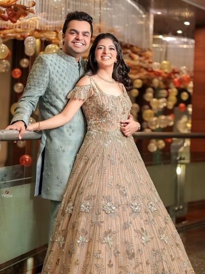 A smiling portrait of the couple, her in a beautiful gown and him in a stylish bandhgala, ready for their engagement party.