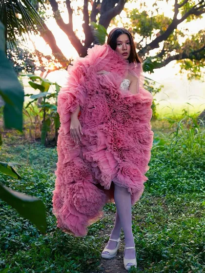 A high-fashion fantasy in pink. Wrapped in a voluminous tulle coat, the makeup is dreamy and ethereal, with a touch of glitter on the eyes to catch the light.