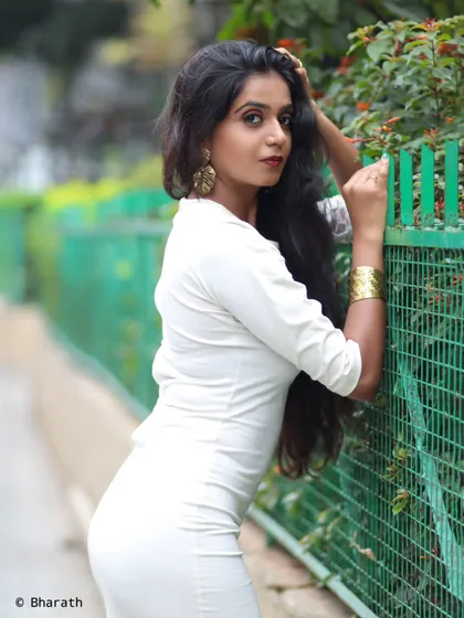 A profile shot of the model in the white dress, leaning against a green fence. This pose accentuates the fit of the dress and the model's long hair.