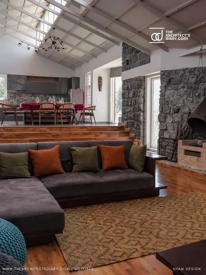The interior living space features a sunken lounge area with a stone fireplace, creating a cozy gathering spot. The split-level design separates the living and dining areas while maintaining a sense of openness under the high, sky-lit ceiling.