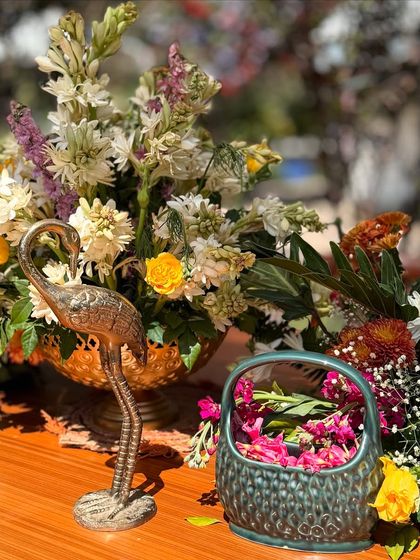 A close up of the festive details for a Holi celebration. A brass flamingo statue sits amongst fresh flowers and a bowl of pink gulal, blending elegant decor with traditional elements.