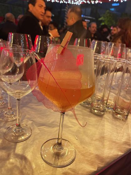 A sparkling cocktail served in a large wine glass, garnished with a translucent, colored leaf. The simplicity of the garnish allows the color and effervescence of the drink to shine.
