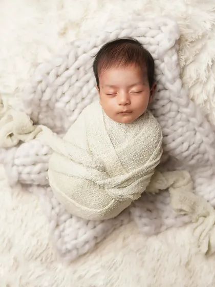 A newborn baby swaddled snugly, sleeping on a fluffy white and grey blanket. This overhead shot emphasizes how small and peaceful they are in their first days.