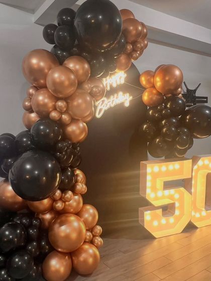 A full view of the black and bronze balloon arch framing the custom birthday backdrop. This type of decor is perfect for making a statement at a milestone celebration.