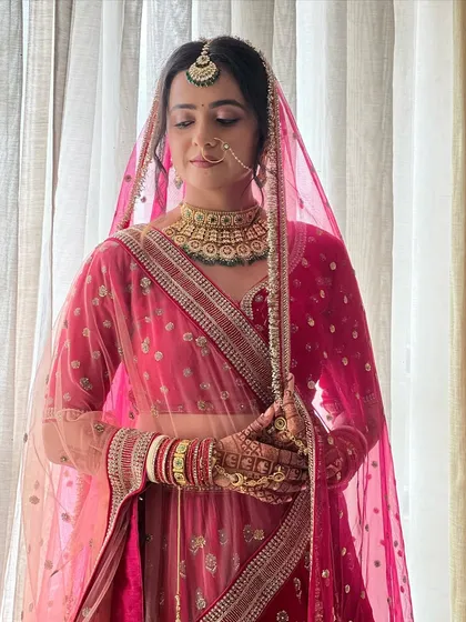 A full-length portrait of the bride, showcasing the beautiful drape of her sheer pink dupatta over the lehenga.