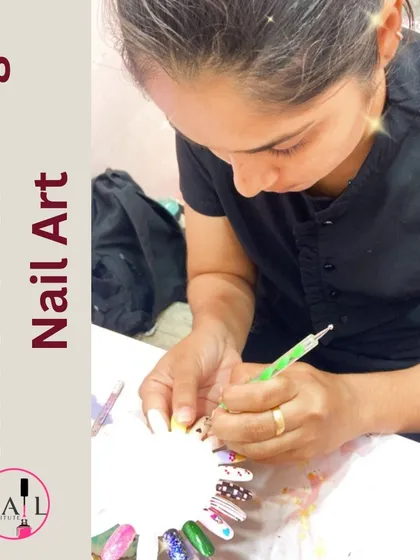 A student focuses on her practice wheel, carefully painting a detailed nail art design.