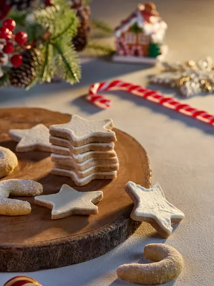 A lovely shot of star-shaped and crescent Christmas cookies on a rustic wooden board. The soft, warm lighting and festive decorations in the background create a gentle and inviting holiday mood for this Marriott Bonvoy shoot.