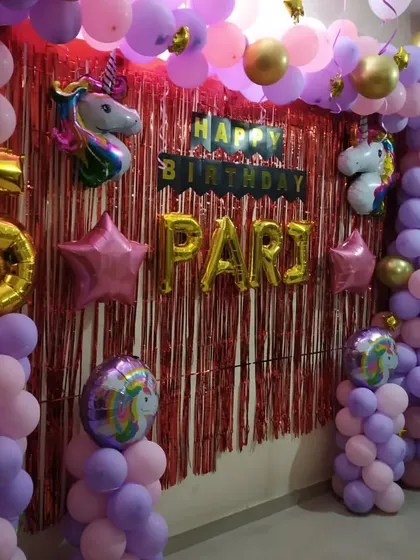 A vibrant Unicorn theme for a 5th birthday party. The decoration uses pink and purple balloons, unicorn foil balloons, and a shimmering red backdrop to create a magical setting.