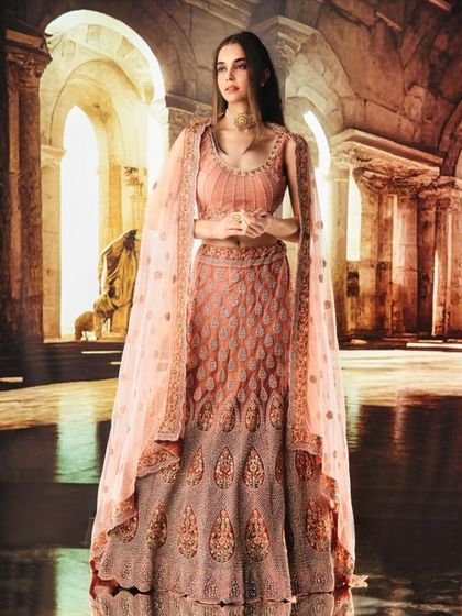 A stunning peach-toned lehenga is set against a projected ancient ruin. The lighting is soft and low, creating a beautiful glow against the awe-inspiring backdrop.