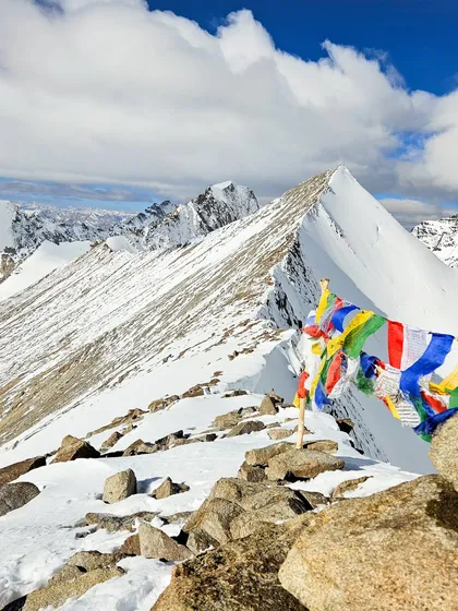 Prayer flags flutter against the stark white of a snowy ridge in Ladakh. In the Himalayas, every climb is also a spiritual journey, a connection to the mountains and the culture that surrounds them.