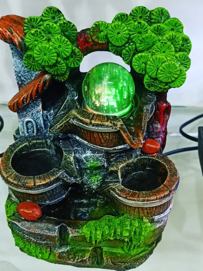 A whimsical tabletop fountain featuring a nature scene with trees and barrels, complete with a color-changing orb.