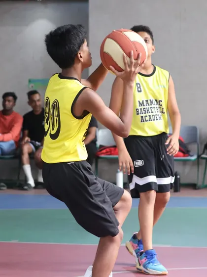 A player practices his shooting form, with a teammate looking on. We foster an environment of mutual support and learning.