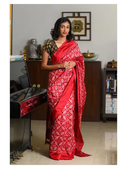 A full-length portrait showcasing a stunning red patterned saree in an elegant indoor setting. The composition, with the piano in the background, adds a touch of classic sophistication to this brand shoot.