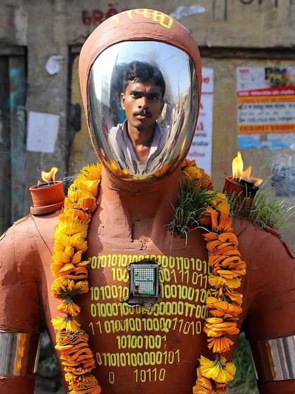 A close-up of a 'Large Language Mystic' shrine, showing a man's reflection in the robot's mirrored face. This invites the viewer to see themselves in the machine.
