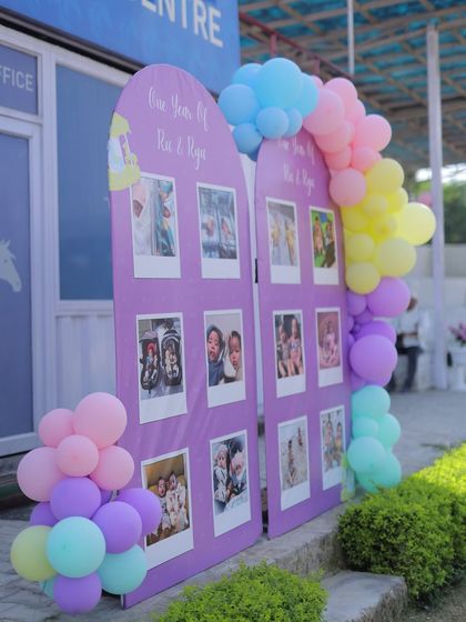 A personalized milestone board designed for twins "Ria & Riya." Shaped like arched windows and decorated with pastel balloon garlands, it showcases a year of memories through adorable polaroid-style photos.